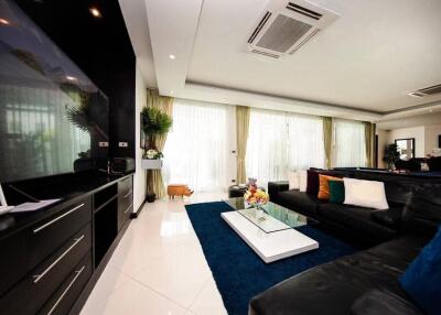 Modern living room with large windows, black leather sofas, glass coffee table, and blue rug