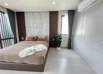 Modern bedroom with double bed, wall-mounted air conditioner, large window, and potted plant