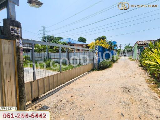 Image showing the entrance gate of a property with a dirt road leading up to it, and surrounding structures and vegetation.