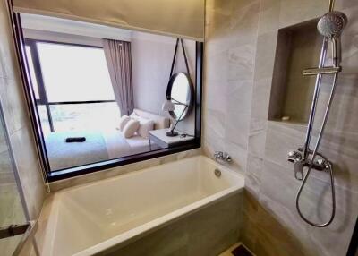 Modern bathroom with bathtub, shower, and window view into bedroom