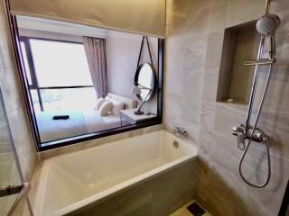 Modern bathroom with bathtub, shower, and window view into bedroom