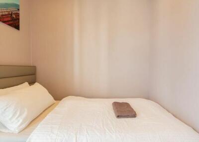 Small bedroom with a bed, white bedding, and a folded towel on top, featuring a modern artwork on the wall.