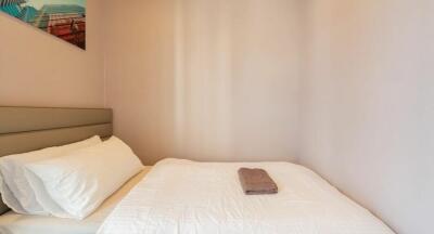 Small bedroom with a bed, white bedding, and a folded towel on top, featuring a modern artwork on the wall.