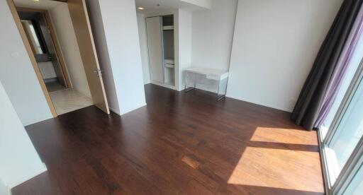 Empty bedroom with wooden floor, closet, and large window with curtains