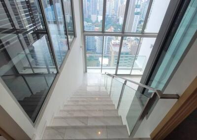 A modern staircase with glass railings leading to a high-rise building view, showcasing large windows and a cityscape.