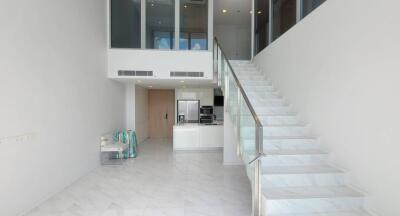 Modern living area with white tiled flooring, staircase, and open kitchen