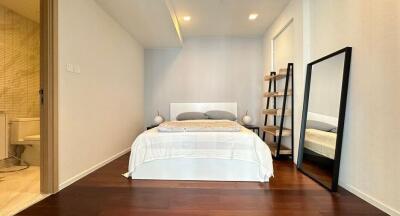 Modern minimalist bedroom with bed, full-length mirror, shelves, and an adjoining bathroom