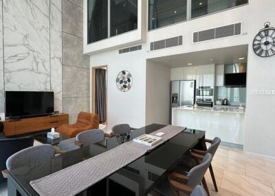 Modern open living area with high ceiling, dining table, and kitchen