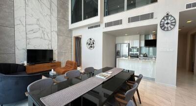 Modern open living area with high ceiling, dining table, and kitchen