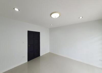 Empty white-walled room with black door and ceiling lights