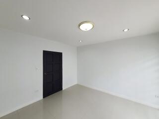 Empty white-walled room with black door and ceiling lights