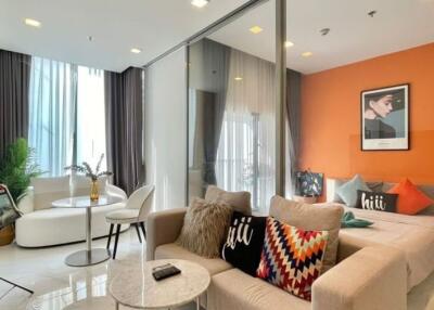 Modern living area with orange accent wall, glass partition, and ample seating