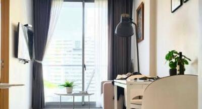 Well-lit living room with a large window, study desk, TV, and potted plant