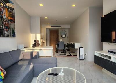 Modern living room with gray sofa, large wall-mounted TV, and a well-lit workspace