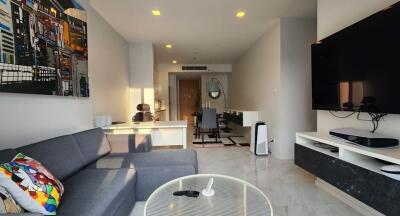 Modern living room with gray sofa, large wall-mounted TV, and a well-lit workspace