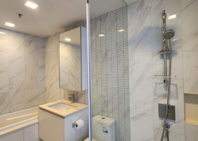 Modern bathroom with marble tiles, bathtub, shower area, and vanity