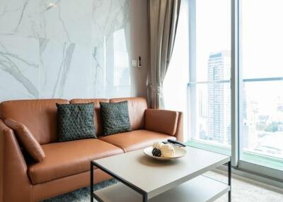 Contemporary living room with a brown leather couch, modern coffee table, large window, and a city view