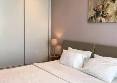 Well-lit bedroom with white bedding, a grey headboard, a nightstand, a lamp, a sliding door closet, and a lion painting.