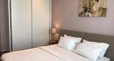 Well-lit bedroom with white bedding, a grey headboard, a nightstand, a lamp, a sliding door closet, and a lion painting.