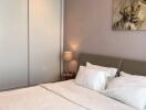 Well-lit bedroom with white bedding, a grey headboard, a nightstand, a lamp, a sliding door closet, and a lion painting.