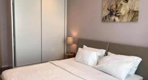 Well-lit bedroom with white bedding, a grey headboard, a nightstand, a lamp, a sliding door closet, and a lion painting.