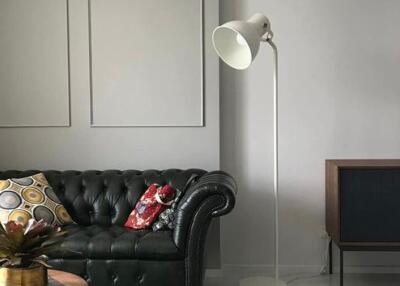 Modern living room with a black leather sofa, floor lamp, and a wooden sideboard