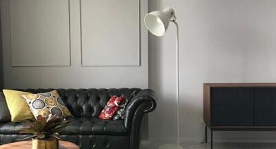 Modern living room with a black leather sofa, floor lamp, and a wooden sideboard