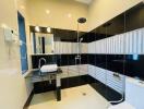 Modern bathroom with black and white tiled walls, shower, sink, and toilet