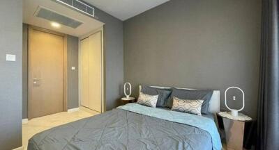 Modern bedroom with gray walls, a wooden door, and a neatly made bed.