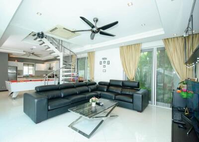 Modern living room with black leather sofas, glass coffee table, pool table, and stainless steel kitchen