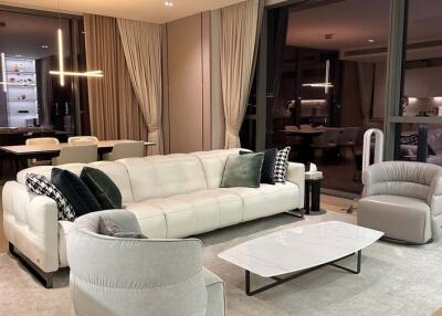 Modern living room with white sofa, chairs, and a coffee table, with dining area in the background.