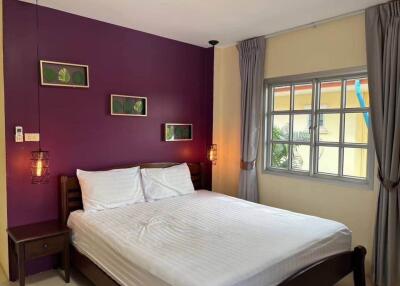 Bedroom with purple accent wall, white bedding, and large window