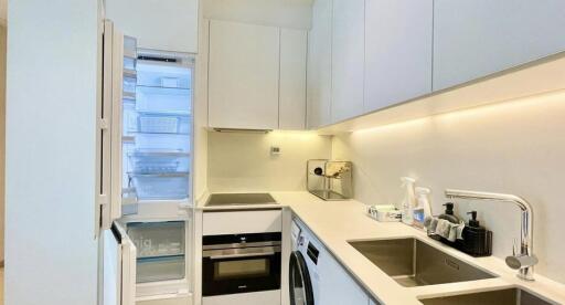 Modern white kitchen with open refrigerator, built-in oven, and washing machine