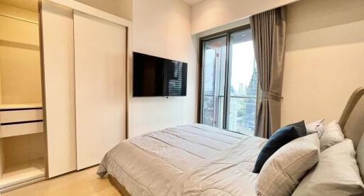 Modern bedroom with a large bed, wall-mounted TV, sliding wardrobe, and a balcony view