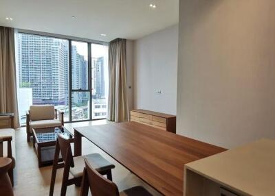 Modern living room with a city view featuring a wooden dining table, chairs, sofa, and large windows