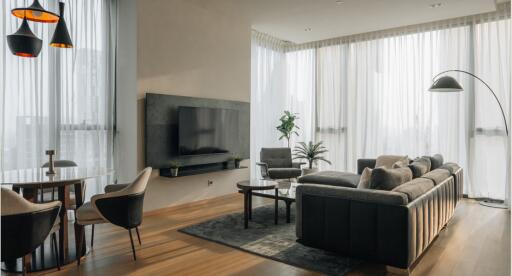 Modern living room with large windows, gray sofas, and a wall-mounted TV