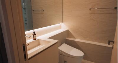 Modern bathroom with beige tiles, a sink with a large mirror, and a toilet