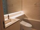 Modern bathroom with beige tiles, a sink with a large mirror, and a toilet