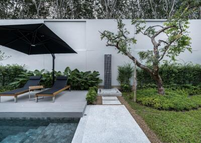 Modern outdoor space with poolside loungers, umbrella, and garden shower