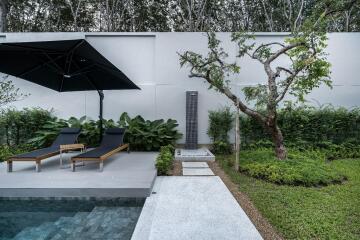 Modern outdoor space with poolside loungers, umbrella, and garden shower
