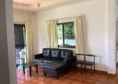 Living room with black leather sectional sofa and window with cream curtains