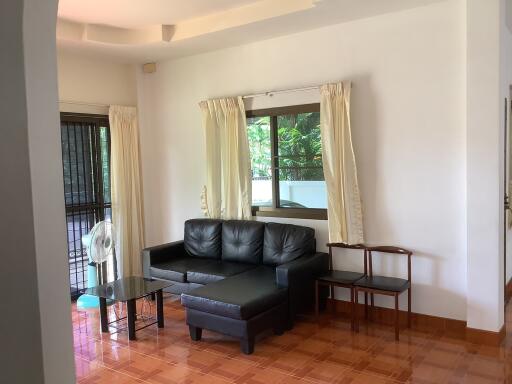 Living room with black leather sectional sofa and window with cream curtains