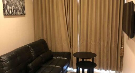 Living room with black leather sofa, two black tables, and beige curtains