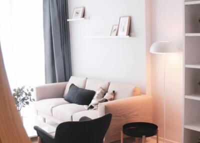 Modern living room with a beige sofa, black armchair, and shelves with decorative items