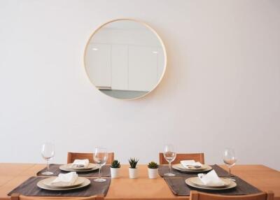 Dining area with a wooden table set for four, featuring a round mirror and minimalist decor