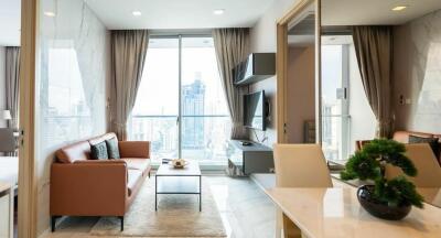 Modern living room with large windows, a brown sofa, a small coffee table, a TV on the wall, and a city view.