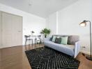 Modern living room with light gray couch, black rug, small dining table, and plants