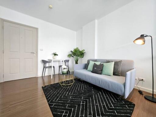 Modern living room with light gray couch, black rug, small dining table, and plants