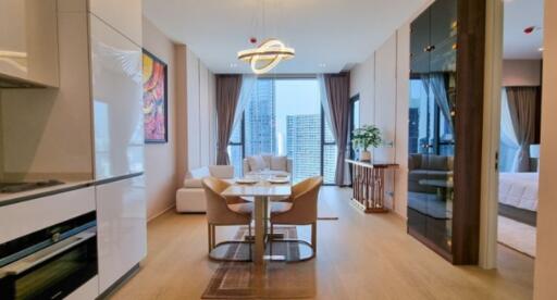 Modern open-plan living area with a dining table, kitchen, and a view of high-rise buildings through large windows