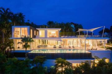 Luxurious modern villa with large glass windows and a swimming pool surrounded by lush greenery at dusk